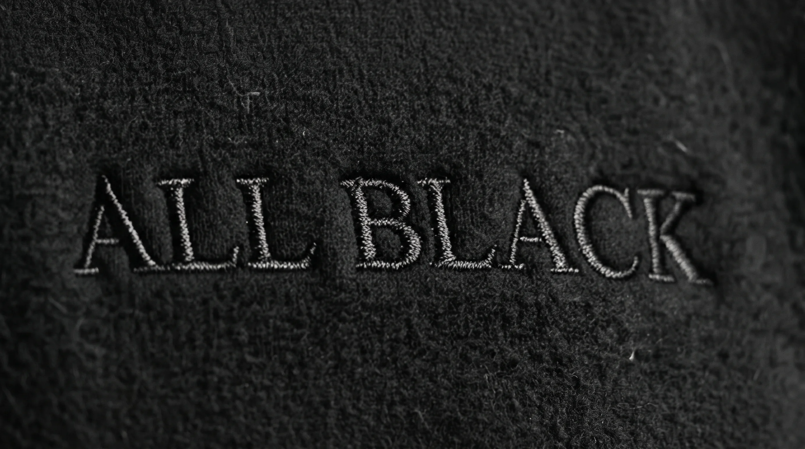 The ALL BLACK wordmark embroidered in dark charcoal thread on black fleece